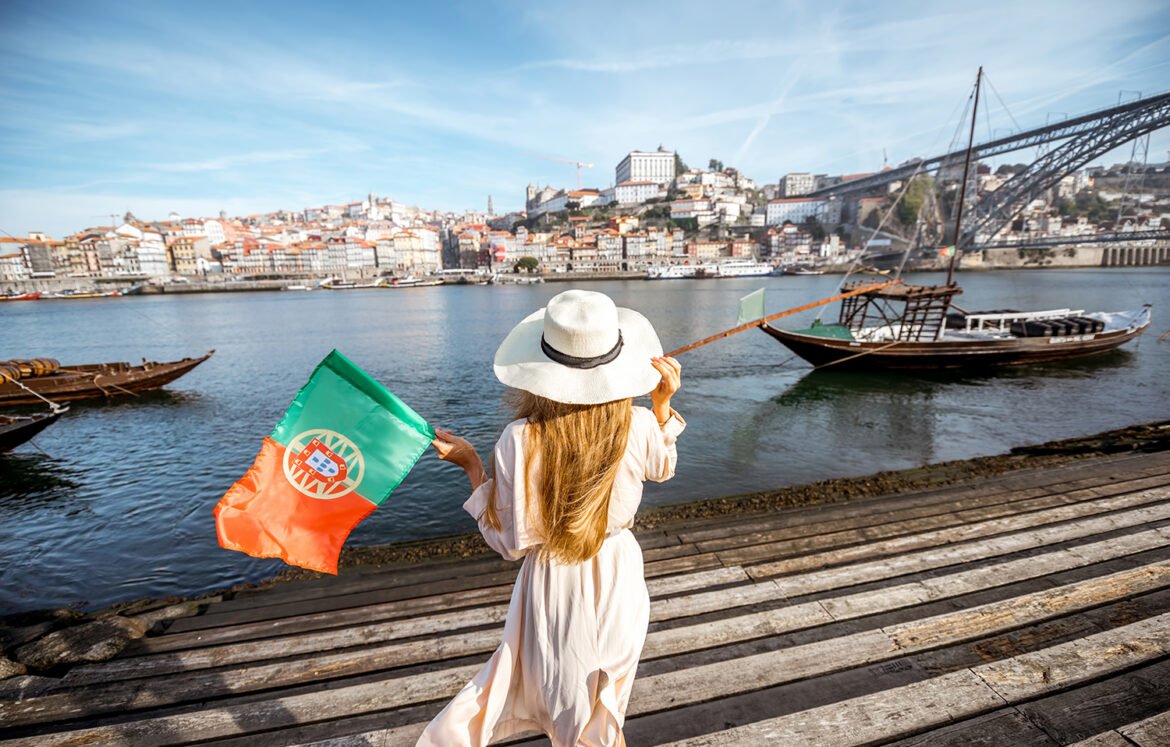 Woman traveling in Porto city Young woman traveler standing back with portuguese flag, enjoying beautiful cityscape view on Douro river and boats during the morning light in Porto, Portugal