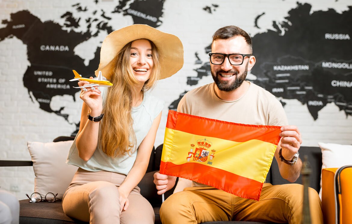 Young couple sitting with spanish flag at the travel agency office on the world map background prepairing for a trip to Spain