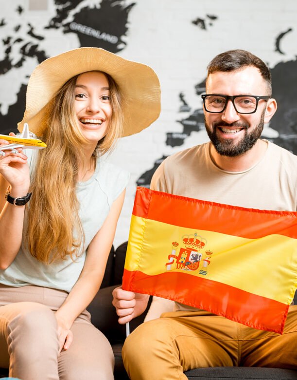 Young couple sitting with spanish flag at the travel agency office on the world map background prepairing for a trip to Spain