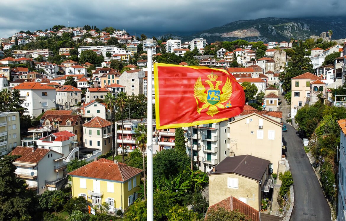 Aerial drone view of the national flag of Montenegro. Town with residential buildings and greenery on the background