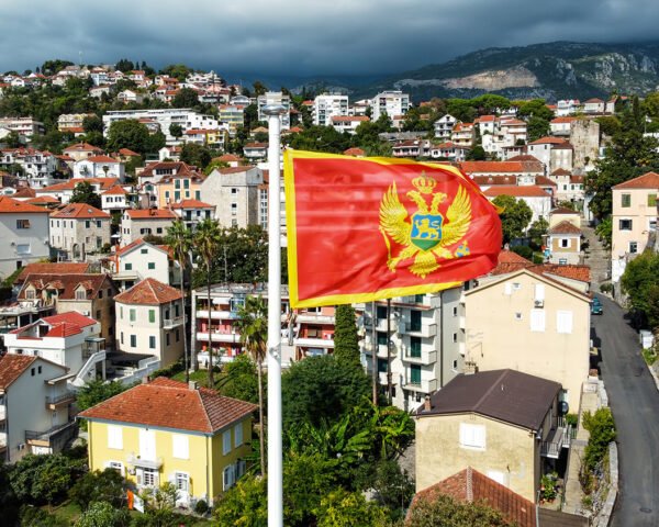 Aerial drone view of the national flag of Montenegro. Town with residential buildings and greenery on the background