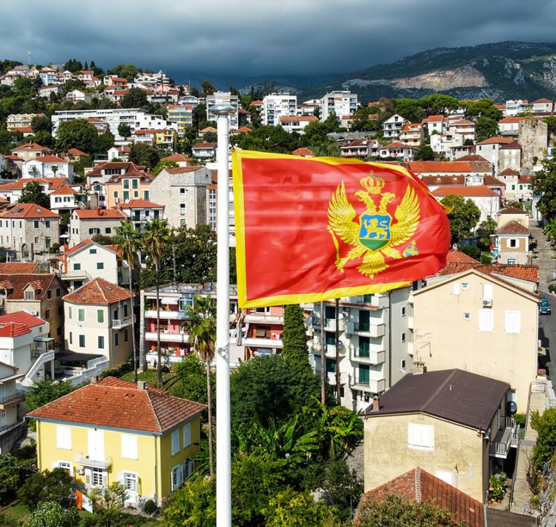 Aerial drone view of the national flag of Montenegro. Town with residential buildings and greenery on the background
