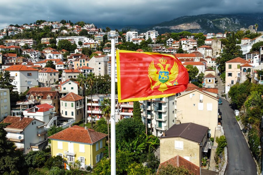 Aerial drone view of the national flag of Montenegro. Town with residential buildings and greenery on the background
